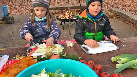 Kinder draußen beim Gemüseschneiden