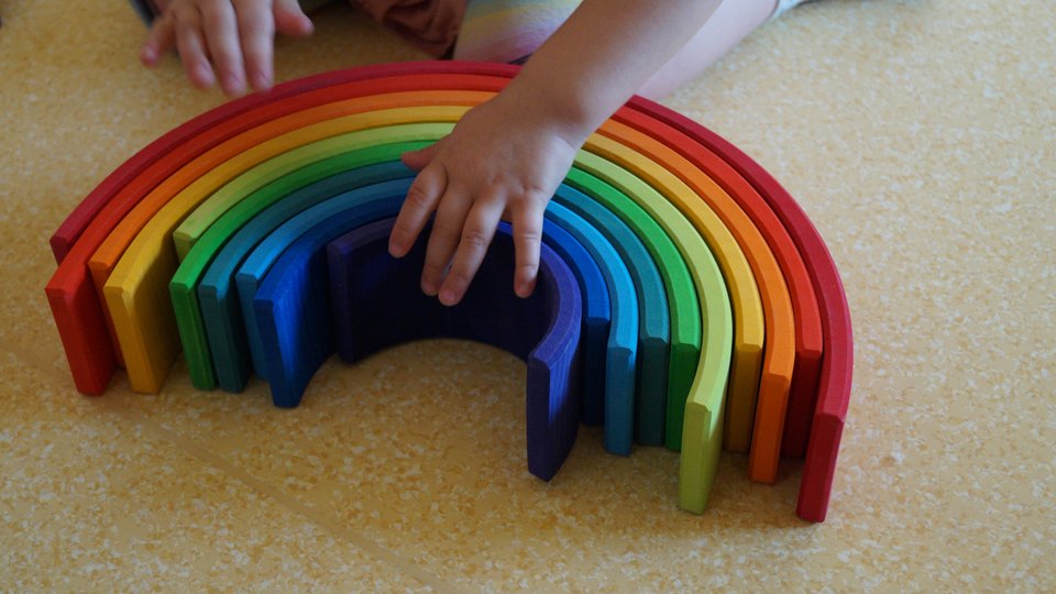 Eine Kinderhand fasst einen Regenbogen aus Holz an.
