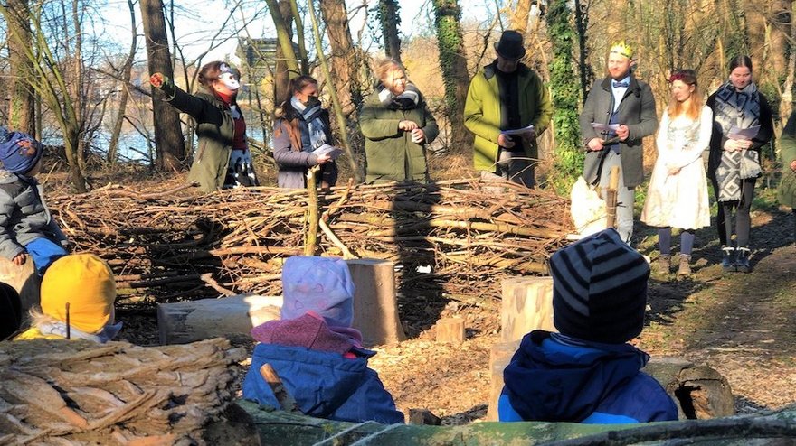 Die Kinder sitzen auf dem Waldsofa und schauen beim Theaterstück zu. 