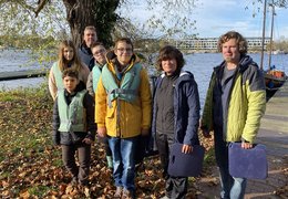 Eine Gruppe Schüler und Lehrer in Jacken und Schutzwesten steht am Ufer 