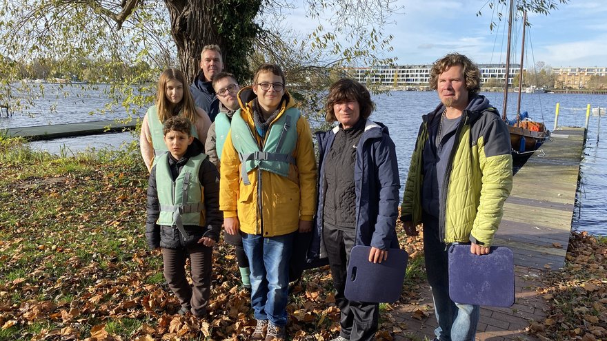 Eine Gruppe Schüler und Lehrer in Jacken und Schutzwesten steht am Ufer 