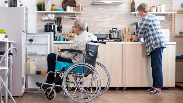 Mann im Rollstuhl und Frau stehend, beide gemeinsam in der Küche