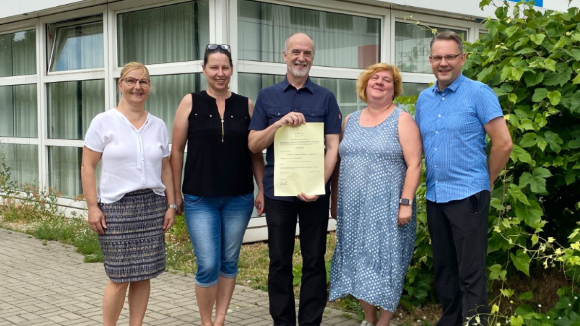 Fünf Menschen stehen mit der Genehmigungsurkunde vor der Schule.