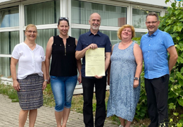 Fünf Menschen stehen mit der Genehmigungsurkunde vor der Schule.