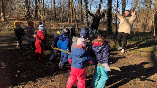 Die Kinder tragen gemeinsam einen großen Stock, den sie im Wald gefunden haben. 
