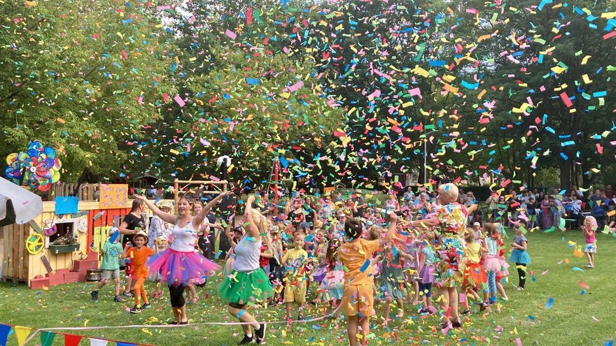 Kinder tanzen auf einer Wiese unter Konfettiregen.