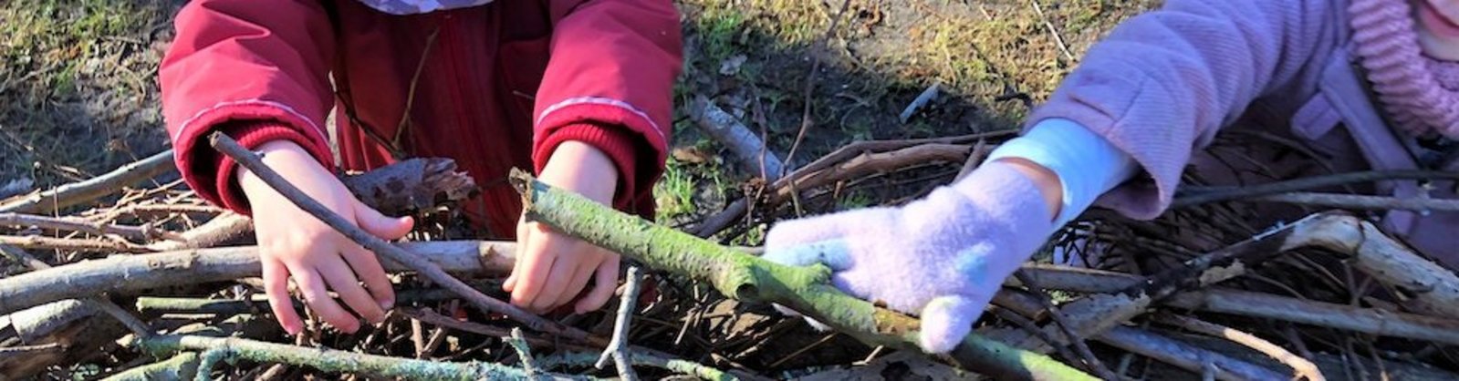 Die Kita-Kinder tragen Stöcke, aus denen das Waldsofa gemeinsam gebaut wird.