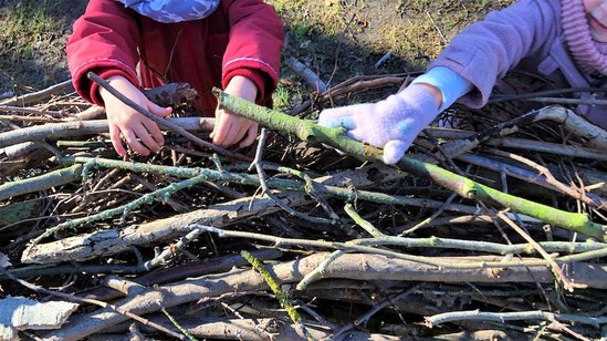 Die Kita-Kinder tragen Stöcke, aus denen das Waldsofa gemeinsam gebaut wird.